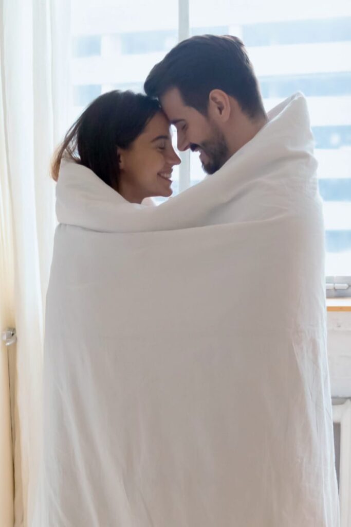 Male and female couple sharing intimacy and pleasure wrapped in a blanket